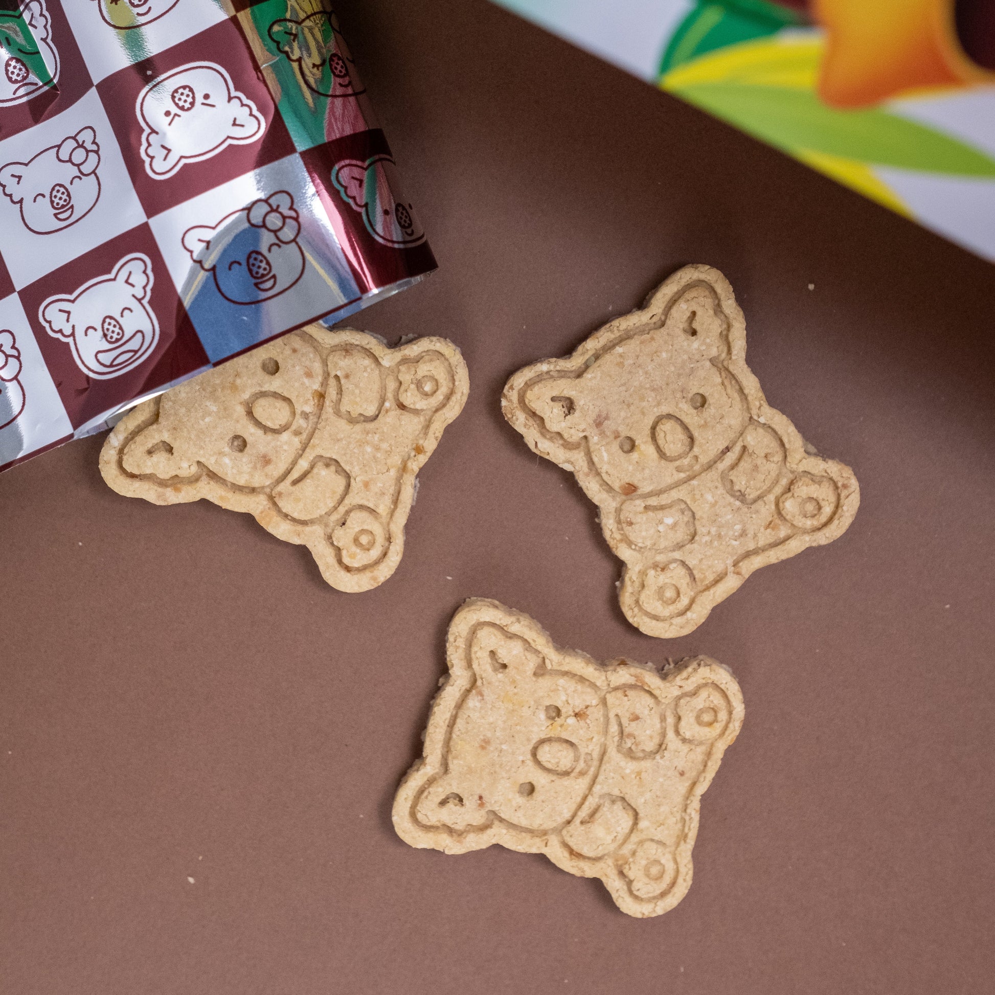 Three bear-shaped cookies on a brown surface with a Lotties Koala box in the background.